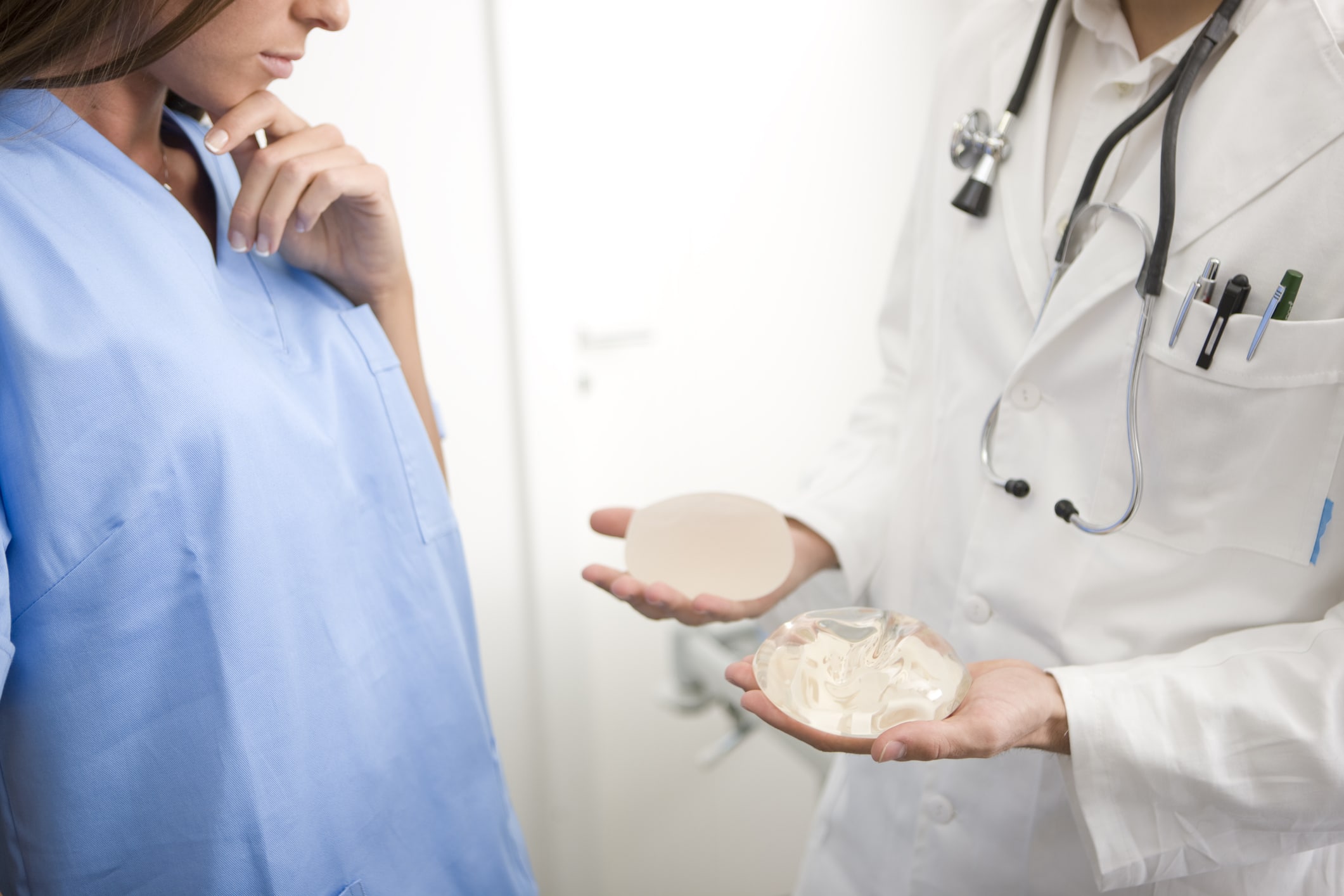 doctor showing patient breast implants, holding one in each hand, one saline, one silicon