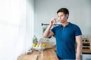 attractive young man stand drinking water and looking out window
