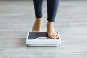 Woman steps on scale to monitor her weight loss progress