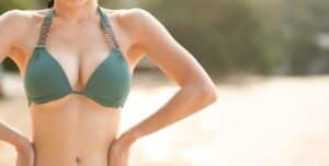 Woman in forest green bikini has proportional breasts after cosmetic surgery.