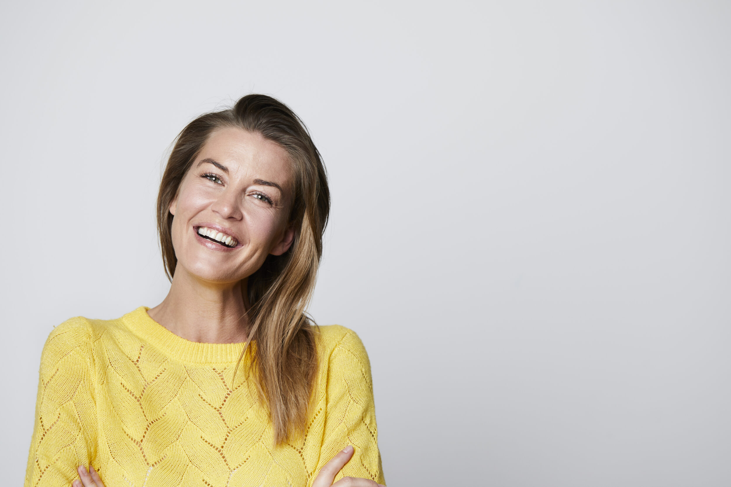 Woman in yellow sweater has a great smile and skin after non-surgical treatments.